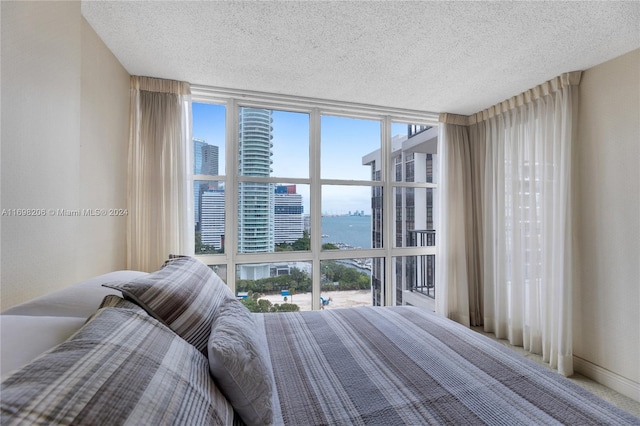 bedroom with expansive windows, a water view, and a textured ceiling