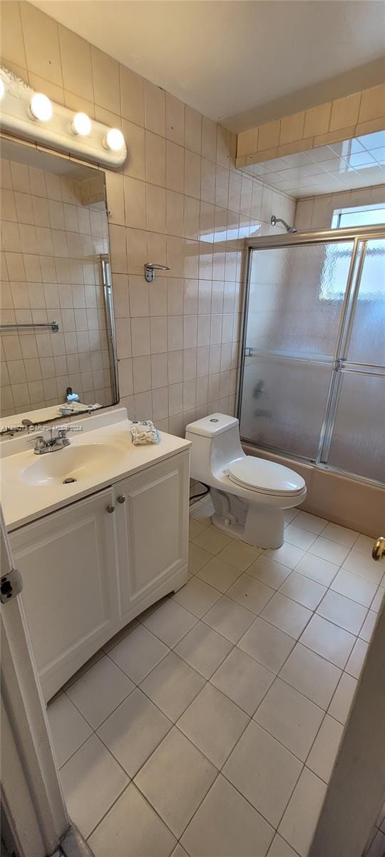 full bathroom with tile patterned floors, vanity, shower / bath combination with glass door, tile walls, and toilet