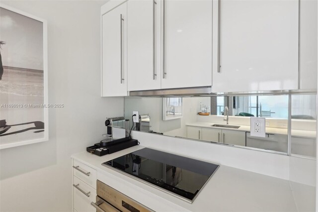 2201 Collins Ave Unit 1015, Miami Beach, FL 33139 - kitchen featuring a sink, black electric cooktop, oven, white cabinetry, and light countertops