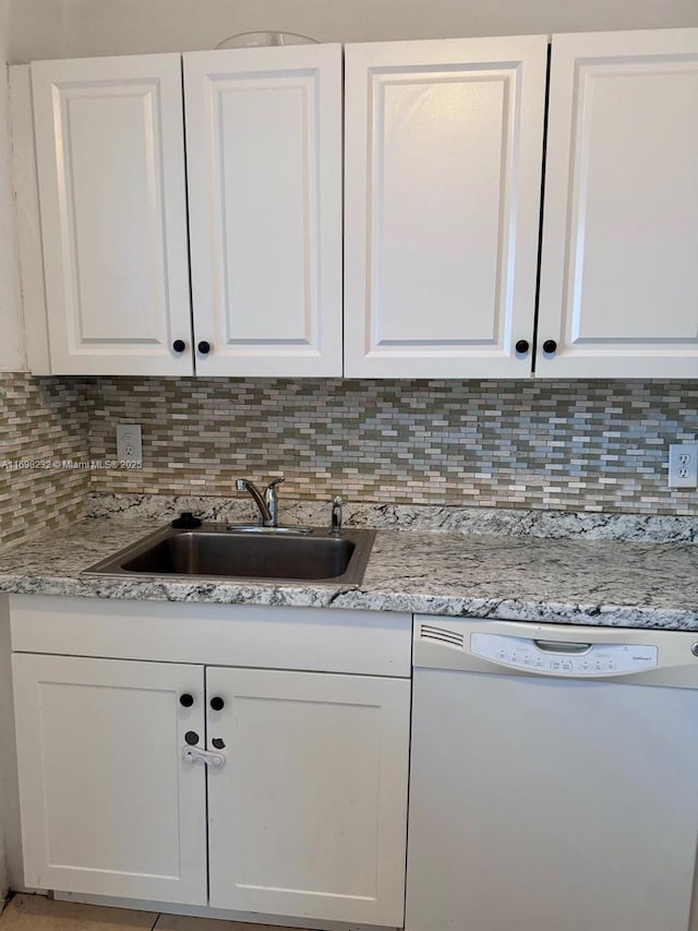 kitchen with white dishwasher, white cabinets, and a sink