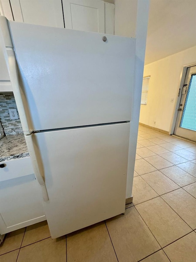 kitchen featuring light tile patterned flooring, decorative backsplash, freestanding refrigerator, and white cabinets