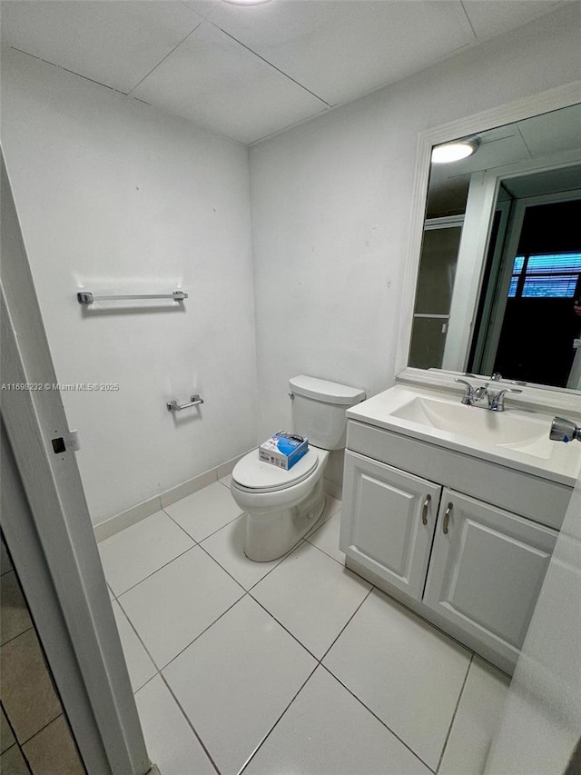 bathroom featuring a paneled ceiling, toilet, vanity, baseboards, and tile patterned floors