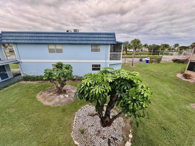 view of side of home featuring mansard roof, a lawn, and a sunroom