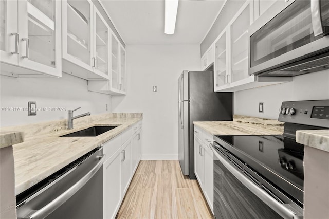 kitchen with light stone countertops, stainless steel appliances, light wood-style floors, white cabinets, and a sink