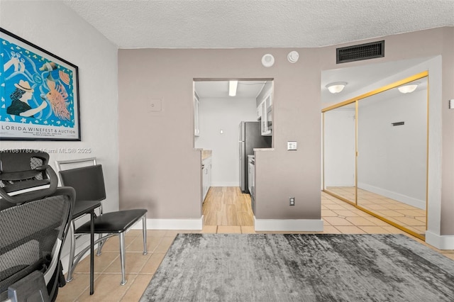 kitchen featuring light tile patterned floors, a textured ceiling, visible vents, and freestanding refrigerator