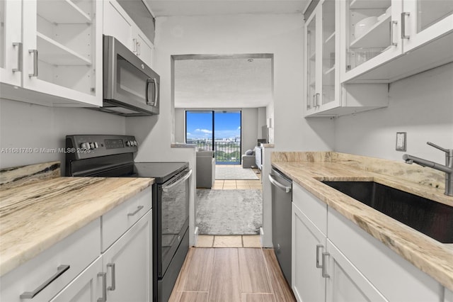 kitchen with stainless steel appliances, a sink, glass insert cabinets, and white cabinetry