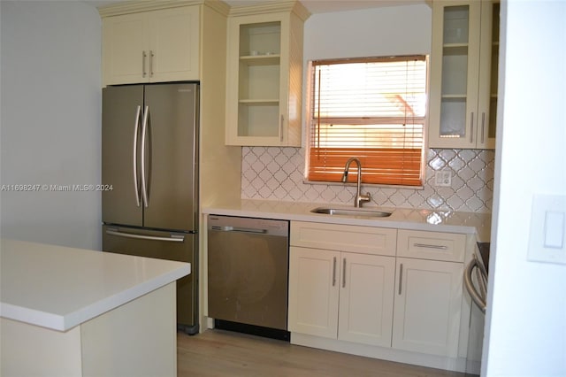 kitchen with appliances with stainless steel finishes, backsplash, light hardwood / wood-style flooring, and sink