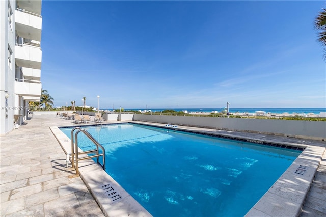 pool with a patio area, a water view, and fence