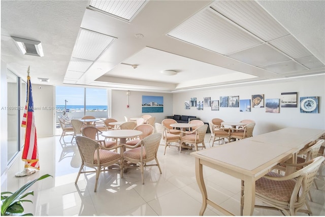 dining space featuring a tray ceiling, floor to ceiling windows, a water view, and light tile patterned floors