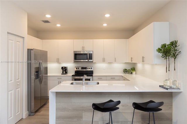 kitchen with kitchen peninsula, a kitchen breakfast bar, stainless steel appliances, white cabinets, and light hardwood / wood-style floors