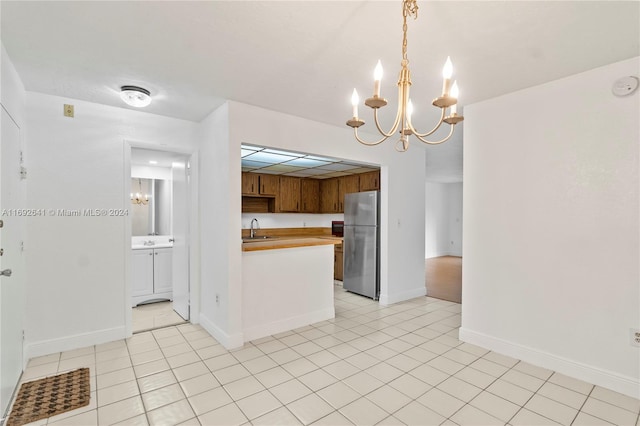 kitchen with stainless steel fridge, light tile patterned flooring, sink, and hanging light fixtures