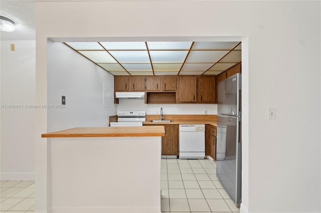 kitchen with sink, kitchen peninsula, white appliances, a paneled ceiling, and light tile patterned flooring