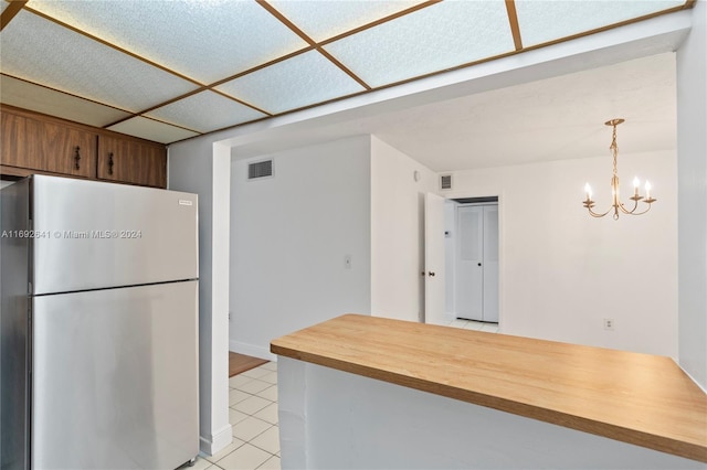 kitchen featuring stainless steel fridge, light tile patterned floors, hanging light fixtures, and a notable chandelier