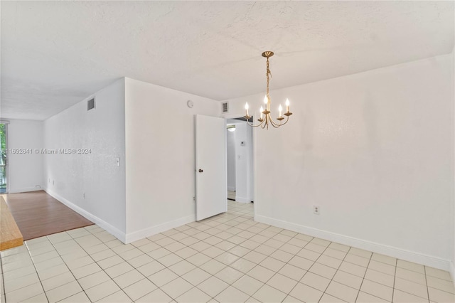 spare room featuring light tile patterned floors, a textured ceiling, and a chandelier