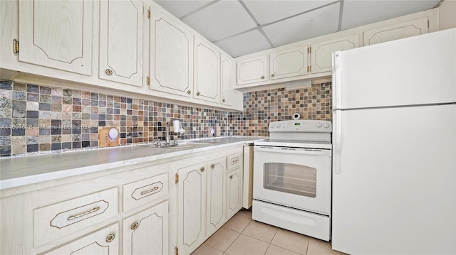 kitchen with a paneled ceiling, white appliances, backsplash, light tile patterned floors, and white cabinetry