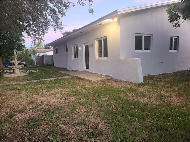 back house at dusk featuring a lawn