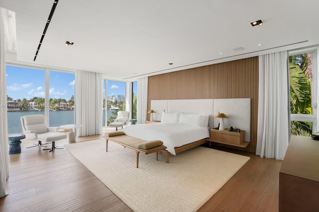 bedroom with hardwood / wood-style floors, a water view, and a wall of windows