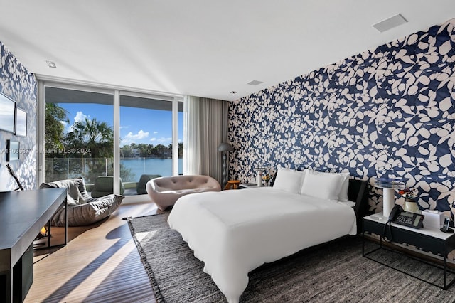 bedroom featuring multiple windows, a water view, and a wall of windows