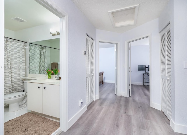 hall with a textured ceiling, light wood-type flooring, and sink