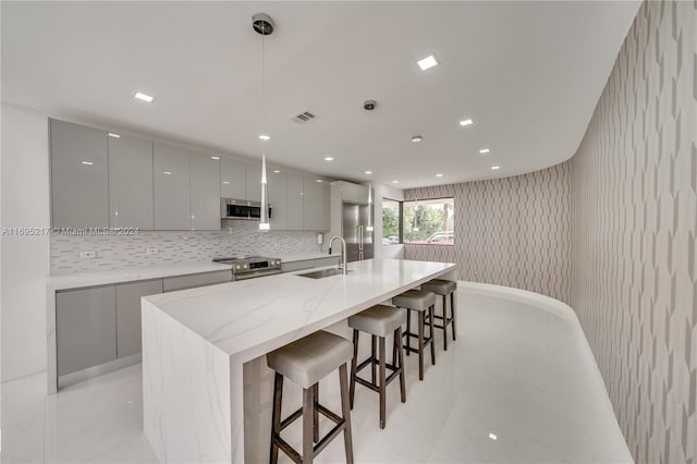 kitchen with gray cabinetry, a breakfast bar, sink, hanging light fixtures, and appliances with stainless steel finishes