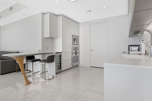 kitchen featuring a breakfast bar area, wine cooler, white cabinetry, and white oven