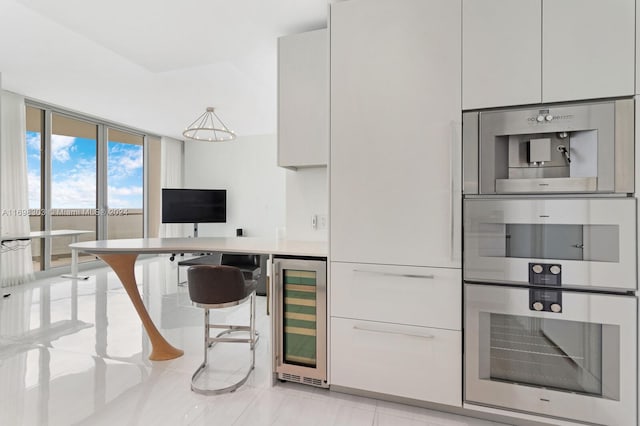 kitchen with white cabinets, double oven, a kitchen bar, and beverage cooler