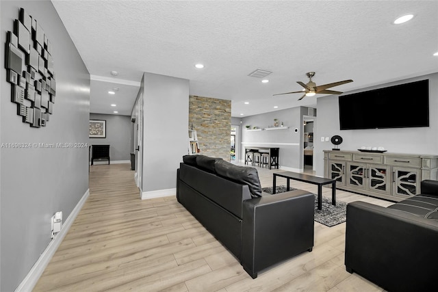 living room with ceiling fan, light hardwood / wood-style flooring, and a textured ceiling