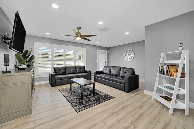 living room featuring a textured ceiling, light wood-type flooring, and ceiling fan