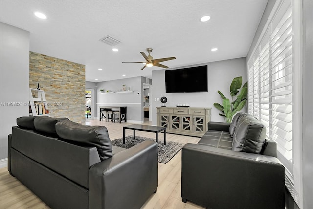 living room featuring ceiling fan, light wood-type flooring, and a textured ceiling