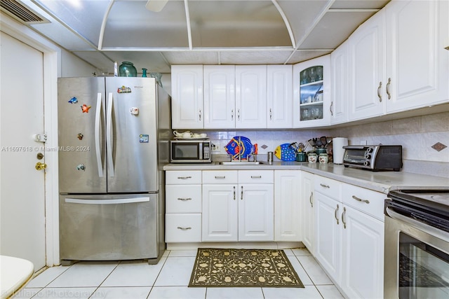 kitchen with tasteful backsplash, white cabinetry, light tile patterned flooring, and stainless steel appliances