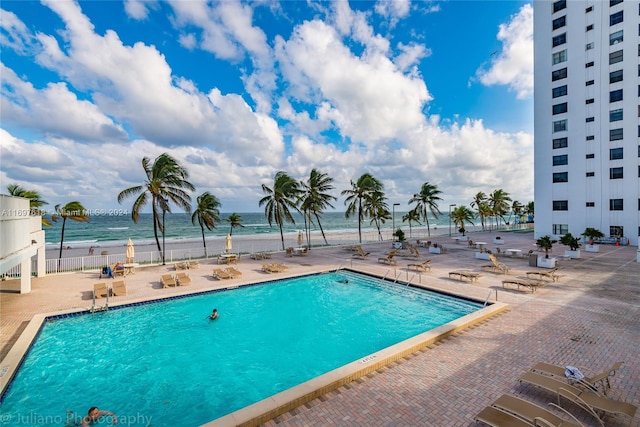 view of swimming pool featuring a water view, a patio, and a beach view