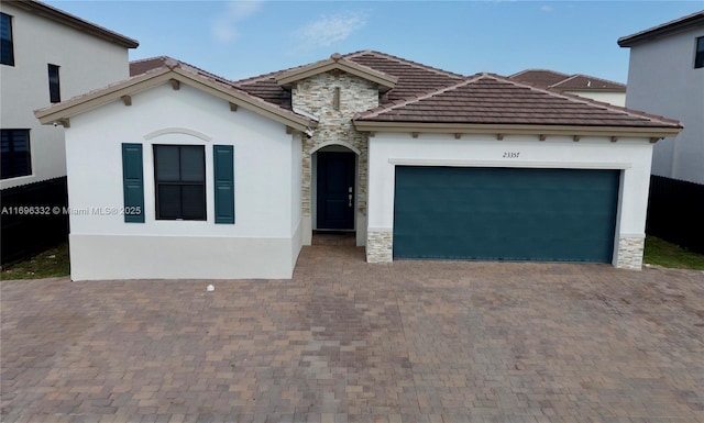 mediterranean / spanish home featuring an attached garage, stucco siding, decorative driveway, and stone siding