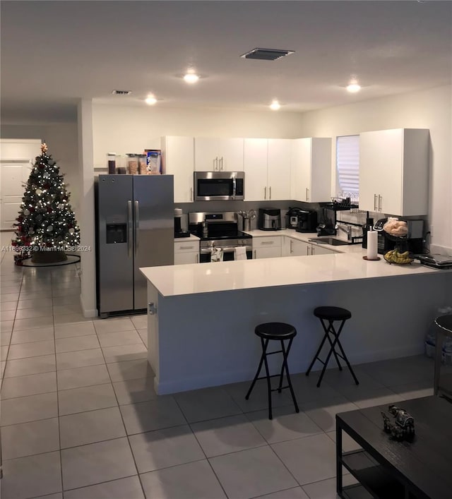 kitchen with white cabinetry, a kitchen breakfast bar, kitchen peninsula, light tile patterned floors, and appliances with stainless steel finishes