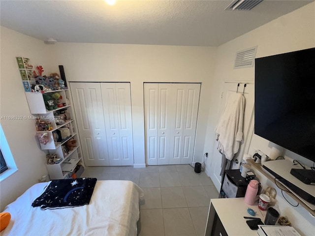 bedroom featuring light tile patterned floors, a textured ceiling, and multiple closets