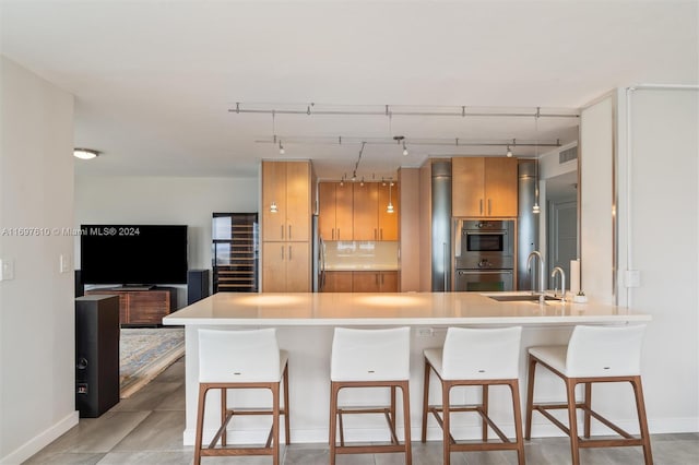 kitchen with kitchen peninsula, stainless steel double oven, a breakfast bar, and sink