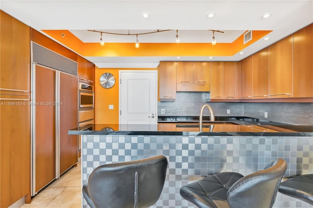 kitchen featuring sink, paneled built in refrigerator, oven, decorative backsplash, and a breakfast bar