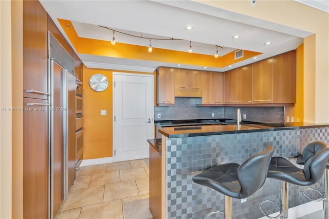 kitchen featuring stainless steel oven, a kitchen breakfast bar, kitchen peninsula, decorative backsplash, and light tile patterned floors