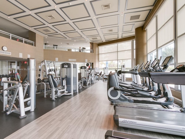 gym featuring a towering ceiling, hardwood / wood-style flooring, and coffered ceiling