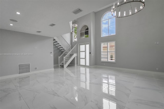 unfurnished living room with a towering ceiling, a textured ceiling, and an inviting chandelier