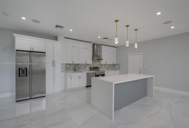 kitchen featuring white cabinets, stainless steel appliances, hanging light fixtures, and wall chimney exhaust hood