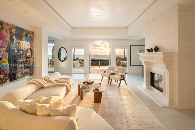 living room with light wood-style floors, a glass covered fireplace, and a raised ceiling