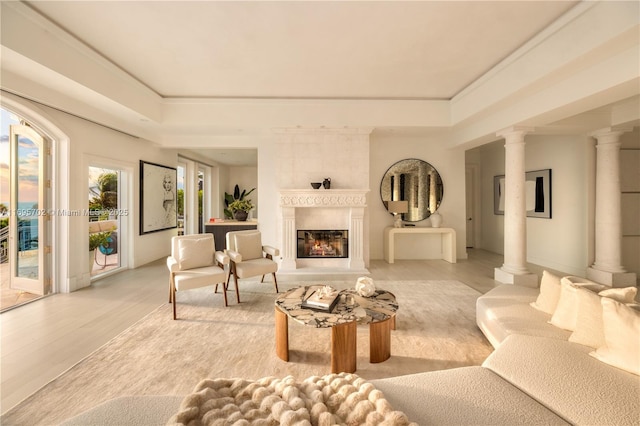 living area with ornate columns, light wood finished floors, and a glass covered fireplace