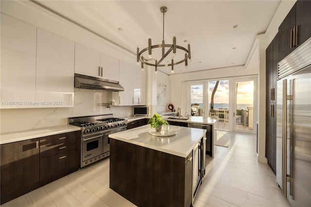 kitchen with under cabinet range hood, white cabinetry, high quality appliances, light countertops, and hanging light fixtures