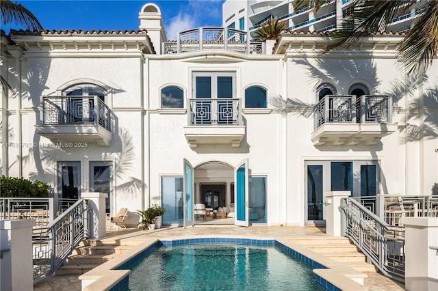 back of property with a balcony, stucco siding, an outdoor pool, and a patio