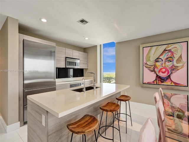 kitchen featuring sink, stainless steel appliances, an island with sink, a kitchen bar, and light tile patterned flooring