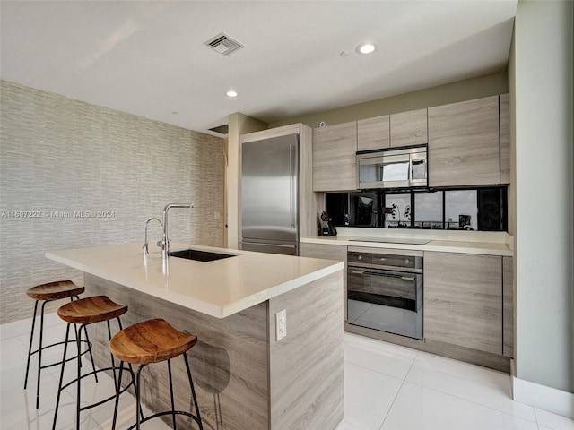 kitchen featuring sink, stainless steel appliances, a kitchen breakfast bar, an island with sink, and light tile patterned floors