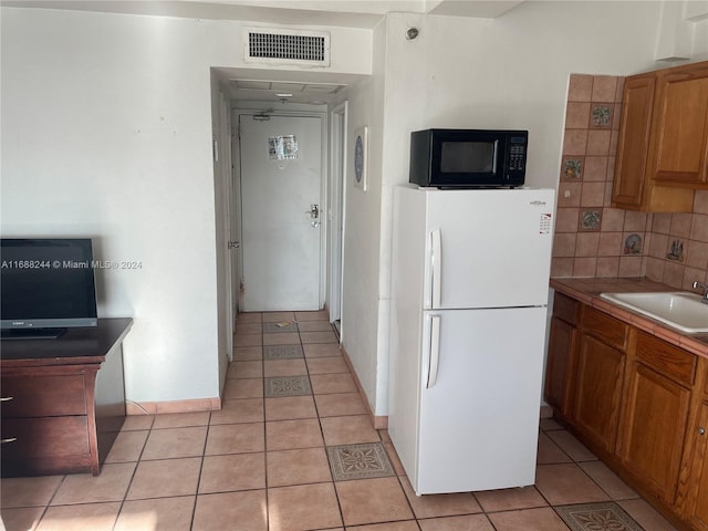 kitchen with white fridge, light tile patterned floors, sink, and tasteful backsplash