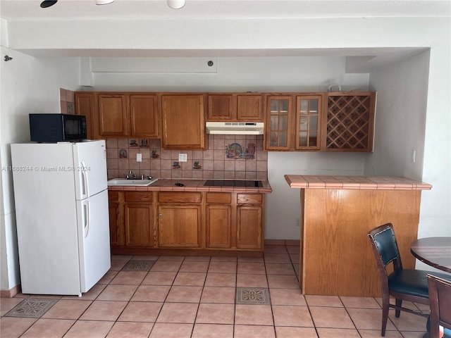 kitchen featuring sink, tile countertops, decorative backsplash, light tile patterned floors, and black appliances