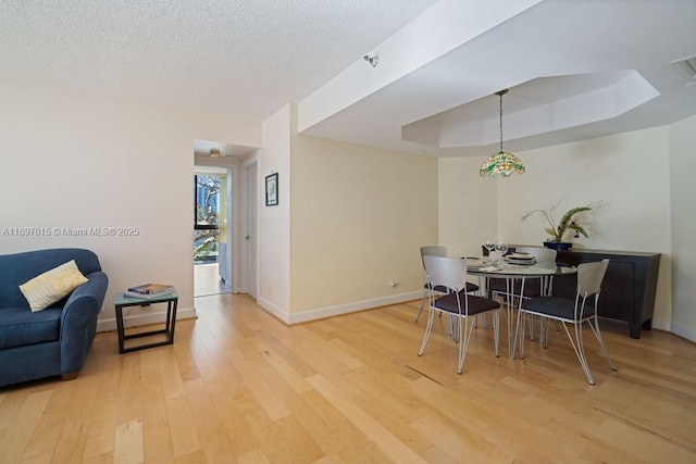 dining area featuring visible vents, baseboards, a tray ceiling, light wood-style flooring, and a textured ceiling