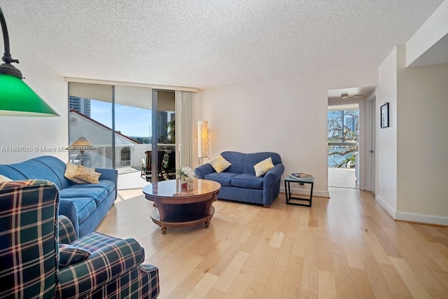 living area with a wall of windows, wood finished floors, baseboards, and a healthy amount of sunlight